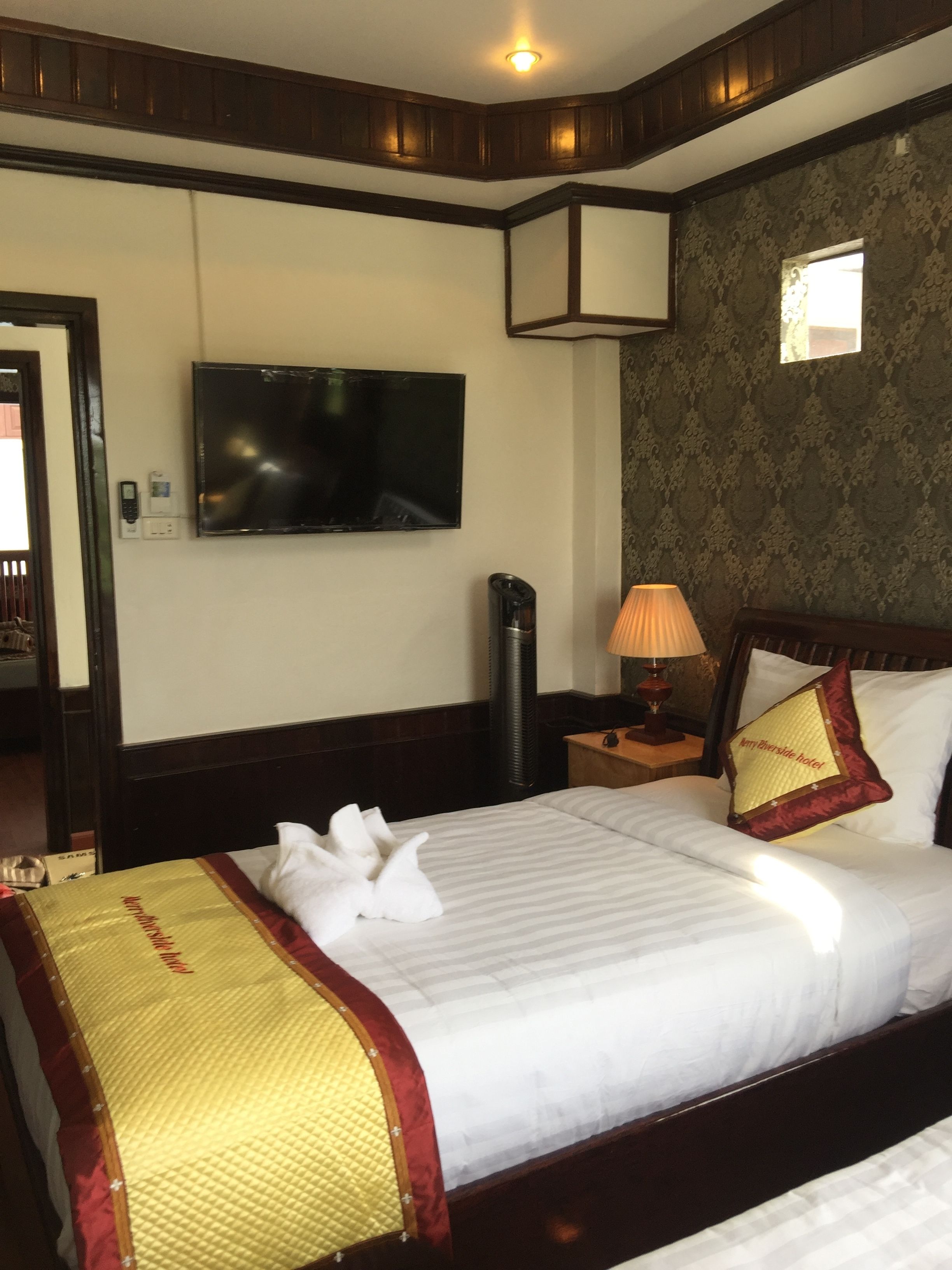A hotel room with a neatly made bed, a television mounted on the wall, and a small window.