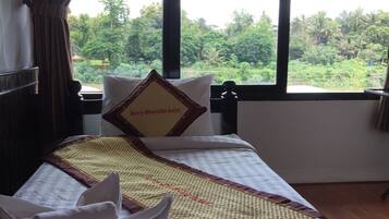A hotel room with a bed, a window with a view of greenery, and a sign on the pillow.