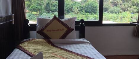 A hotel room with a bed, a window with a view of greenery, and a sign on the pillow.