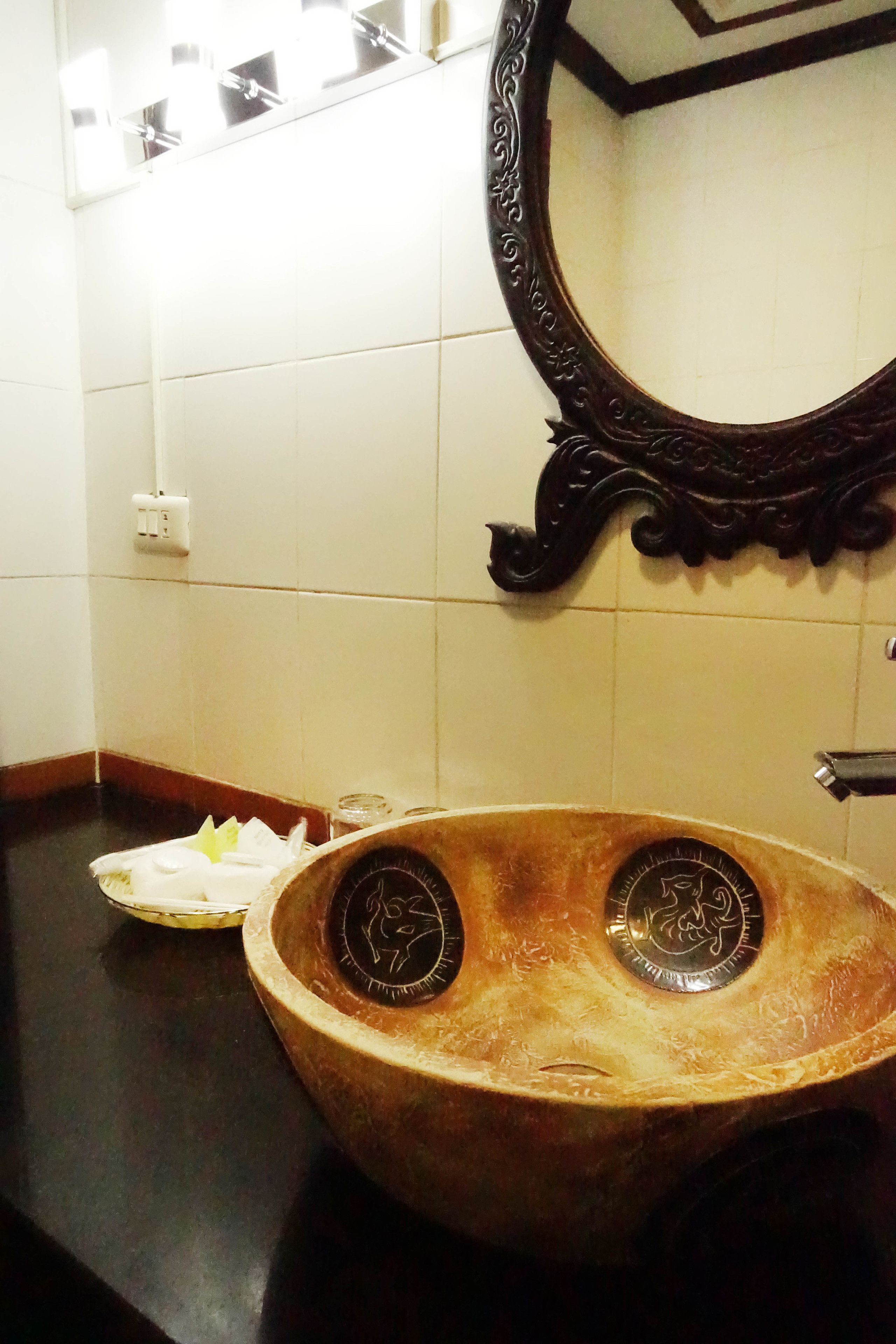 Ein Badezimmer mit einem großen, verzierten Spiegel, einem hölzernen Waschbecken mit zwei Wasserhähnen und einem weißen Handtuch auf der Ablagefläche.