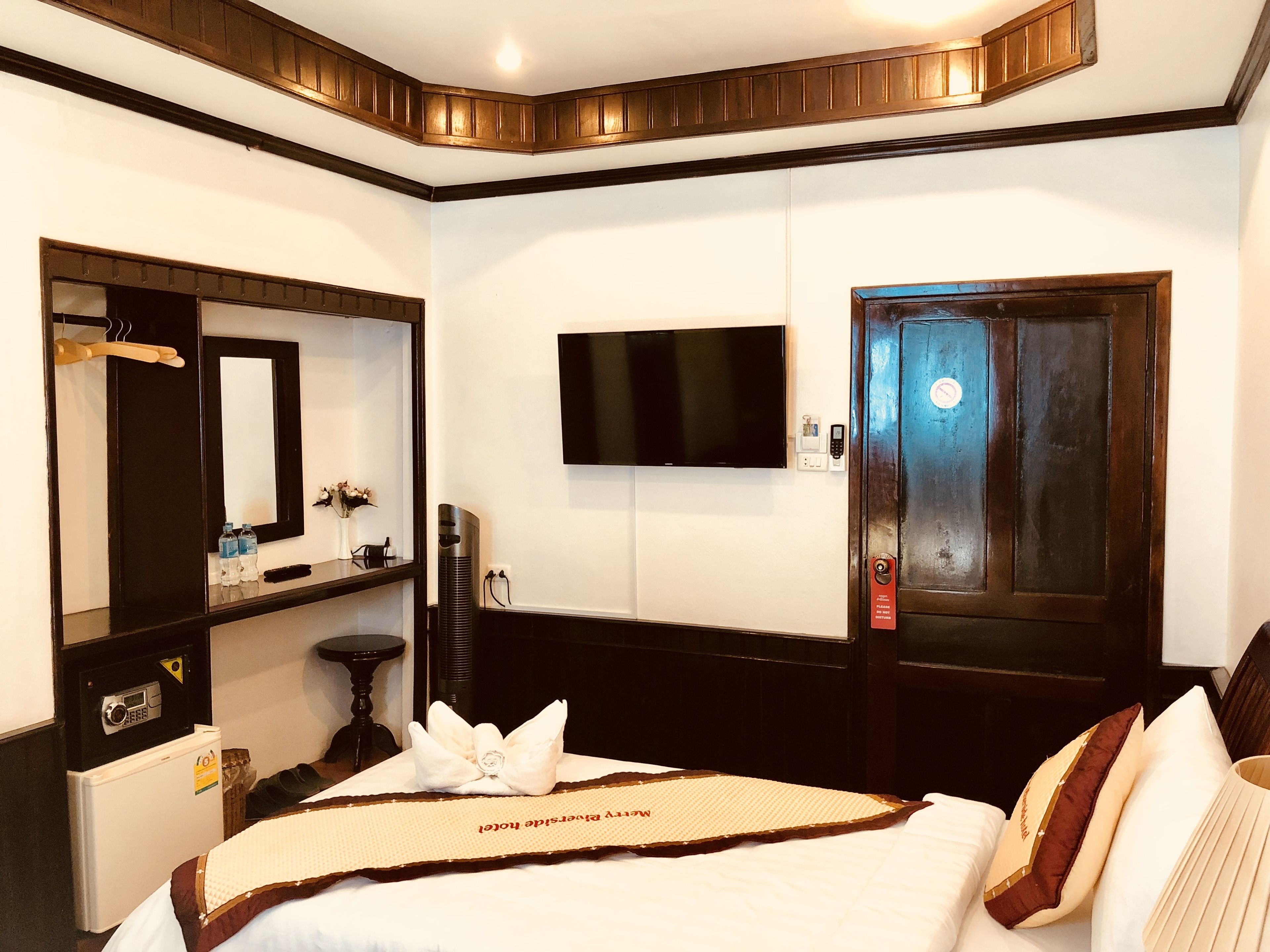 Une chambre d’hôtel comprenant un lit, un téléviseur fixé au mur, une porte dotée d’une serrure de sécurité, une petite table avec un vase et un miroir.