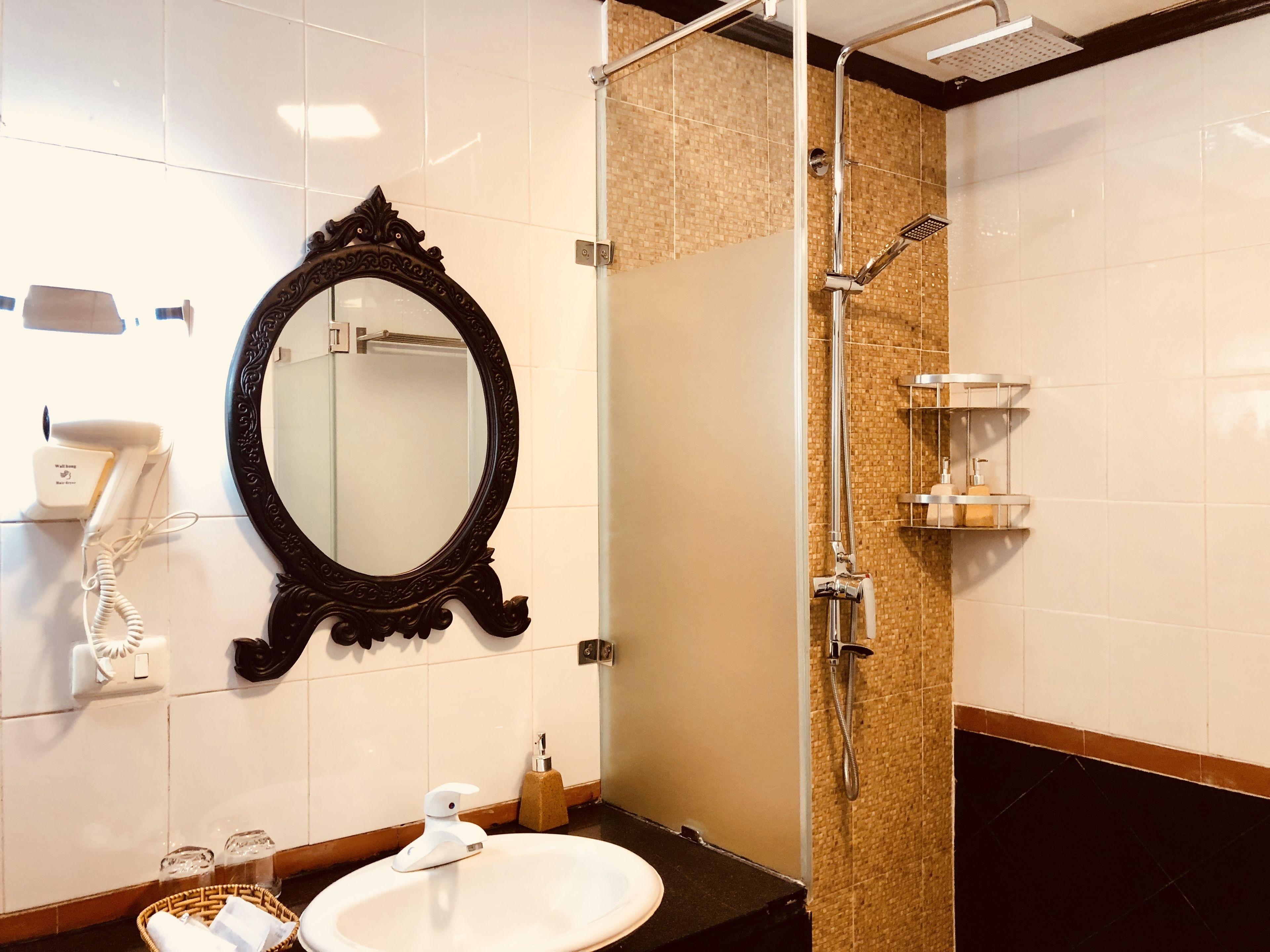 A bathroom with a large ornate mirror, a white sink, a glass shower enclosure, and a towel rack.