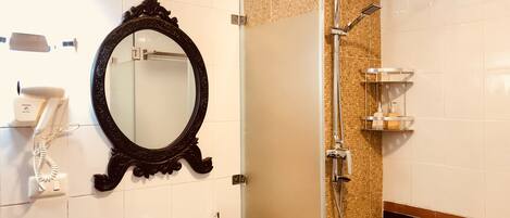 A bathroom with a large ornate mirror, a white sink, a glass shower enclosure, and a towel rack.