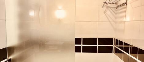A modern bathroom with a glass shower enclosure, black and white tiled walls, and a wooden ceiling.