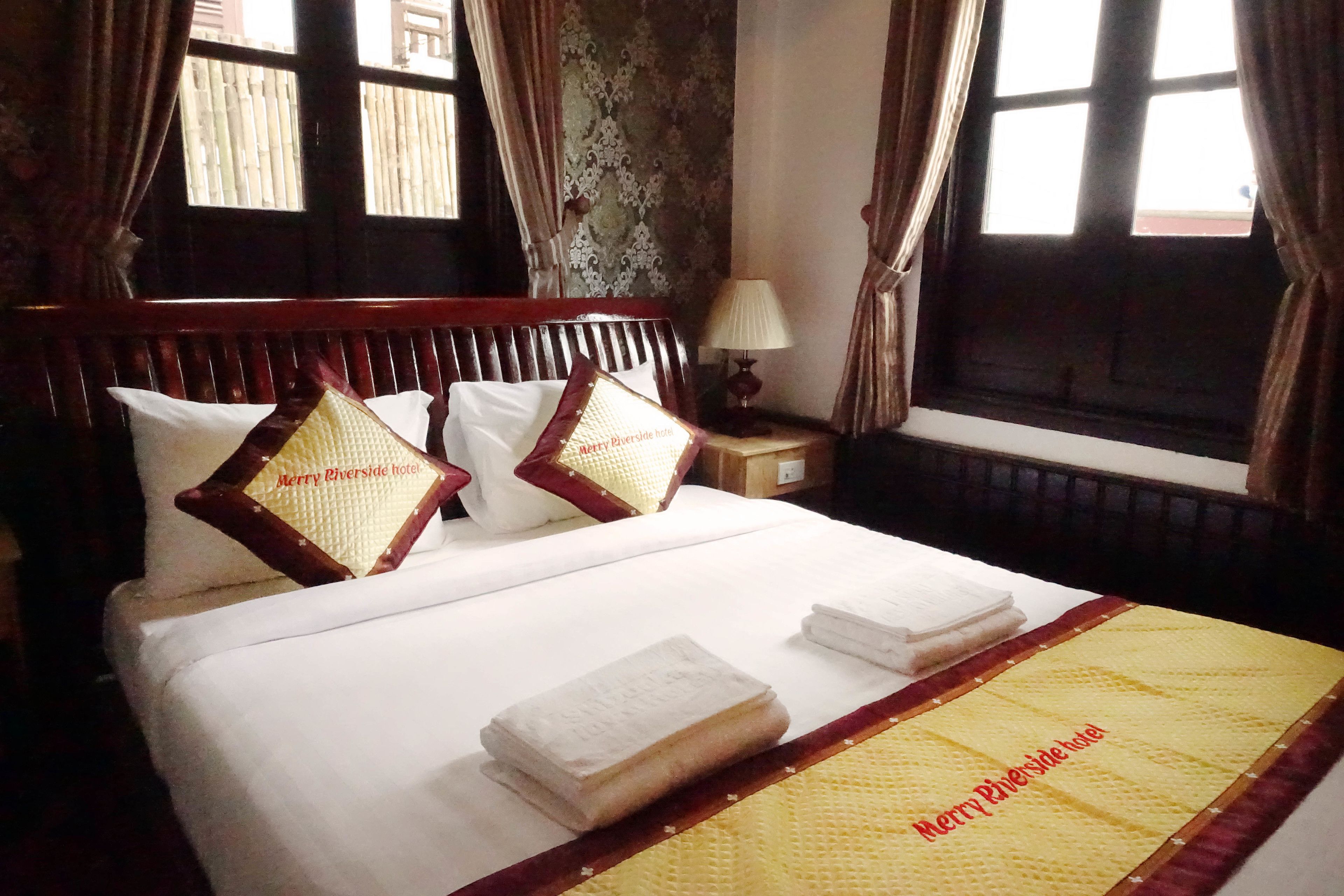 A hotel room with a bed, pillows, a bedside table with a lamp, and a window with curtains.