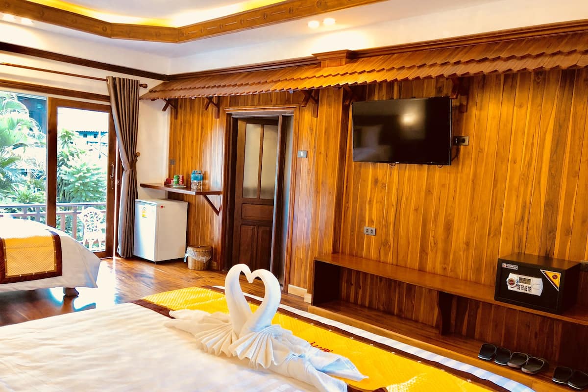 A hotel room with a bed, a TV mounted on the wall, a wooden floor, and a balcony with plants.