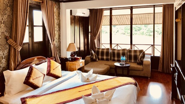 A hotel room with a bed, a sofa, a small table with a lamp, and a window with curtains. - Merry Riverside Hotel (Luang Prabang)