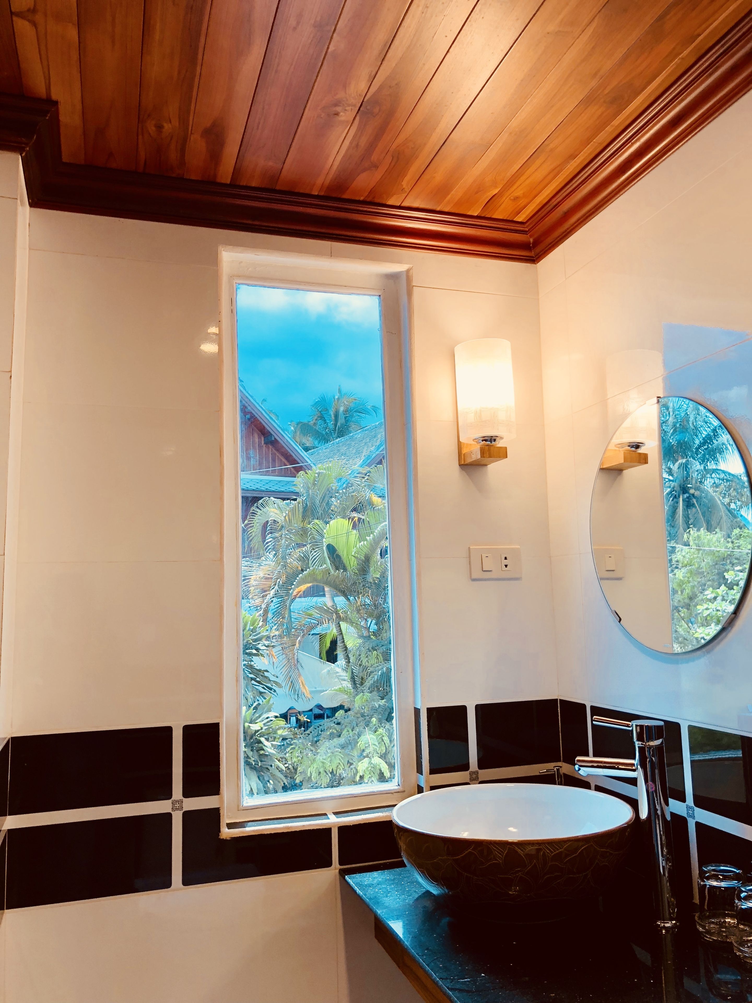 Un bagno con un'ampia finestra, uno specchio tondo e un lavabo a vasca.