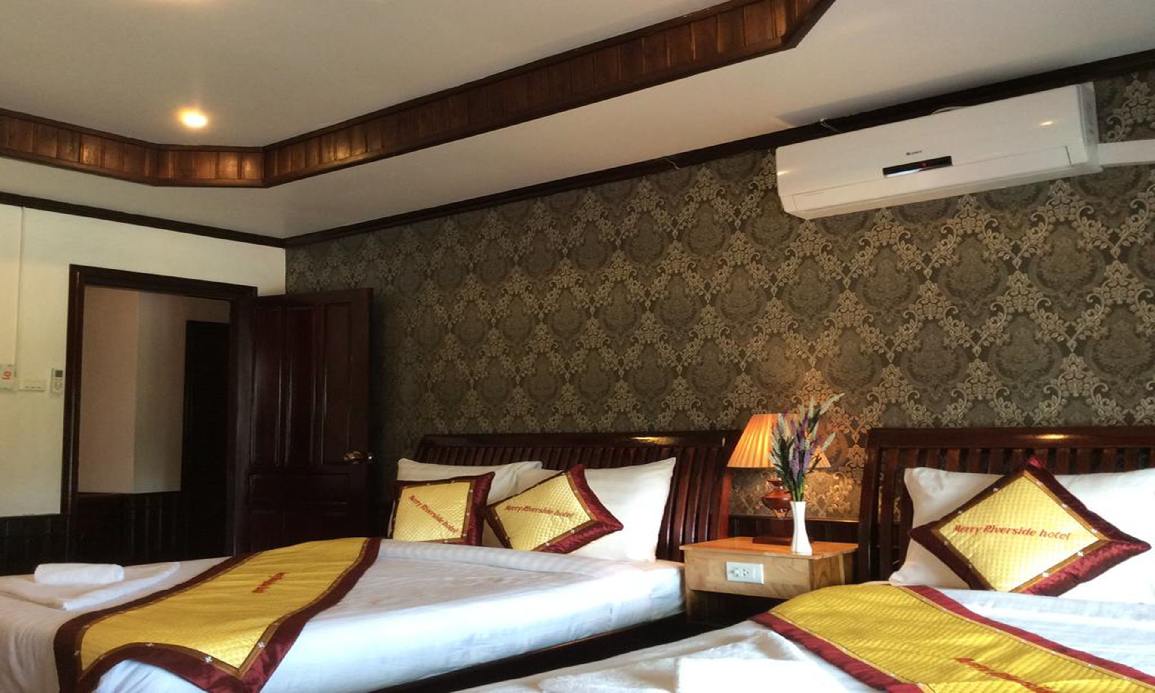 A hotel room with two beds, a wooden headboard, a patterned wallpaper, and an air conditioning unit.