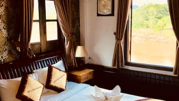 Hotelkamer met een groot bed, nachtkastje met lamp, raam met gordijnen en uitzicht op groen.
