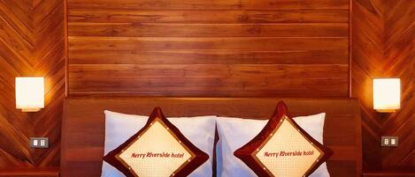 Habitación de hotel con cabecera de madera, dos almohadas con el nombre del hotel, cama con colcha azul y blanca a cuadros, y dos luces fijadas en la pared.