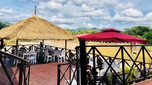 An outdoor seating area with thatched and red umbrellas, wooden tables, and chairs. - Merry Riverside Hotel (Luang Prabang)