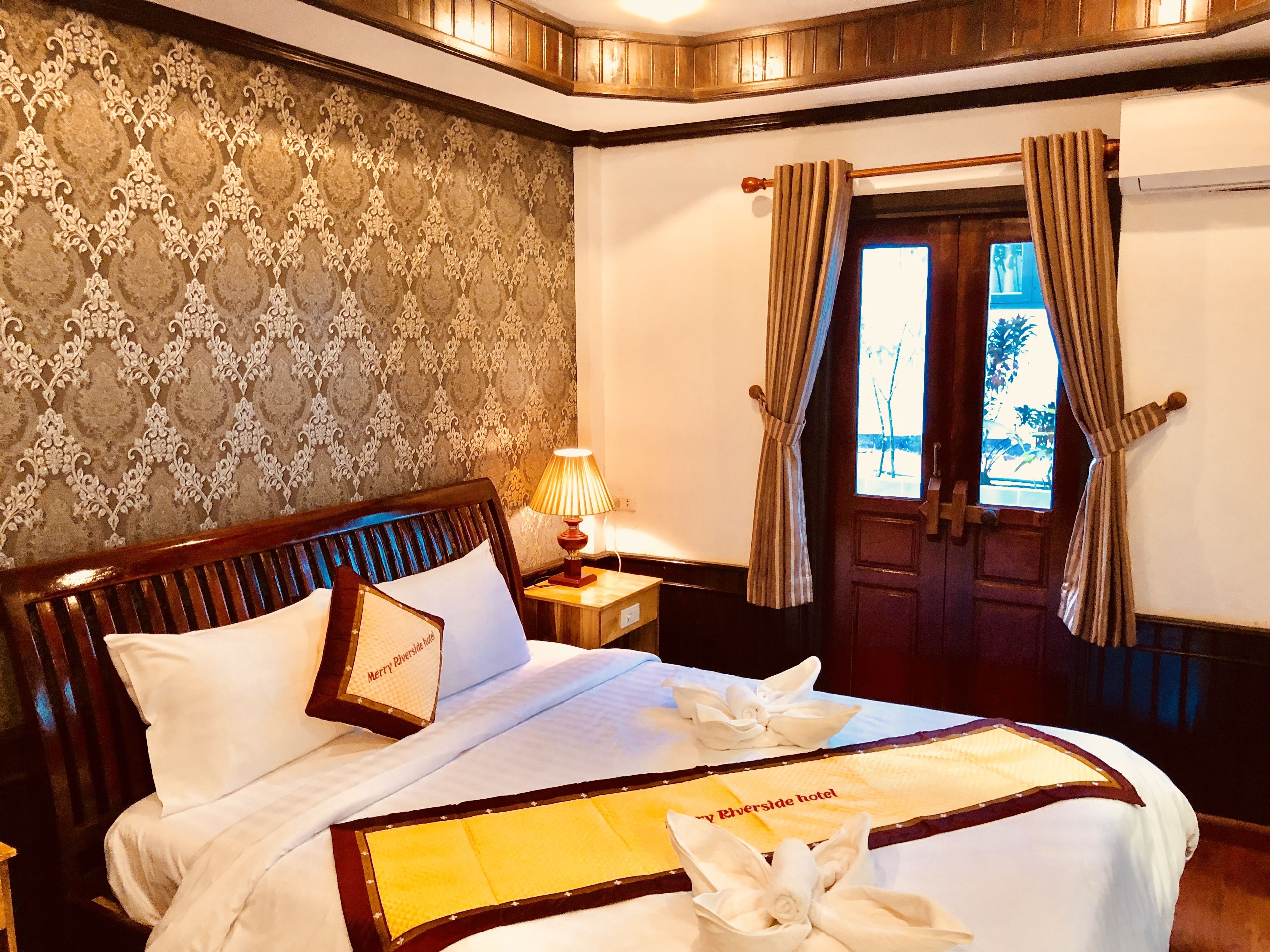 A neatly made bed with a headboard, a bedside lamp, and a window with curtains.