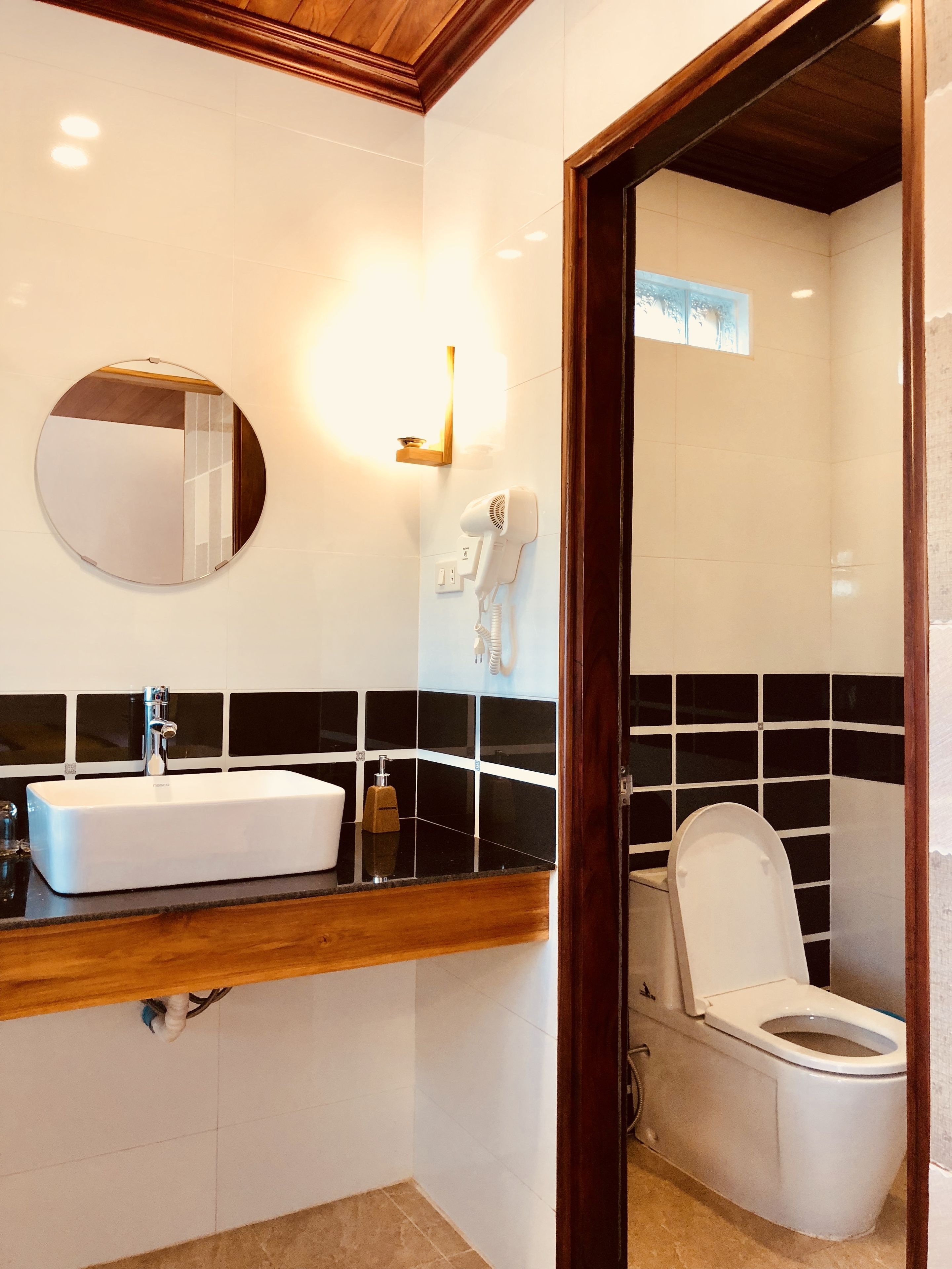Un baño moderno con un lavabo blanco, un espejo redondo, un secador de pelo y un inodoro.