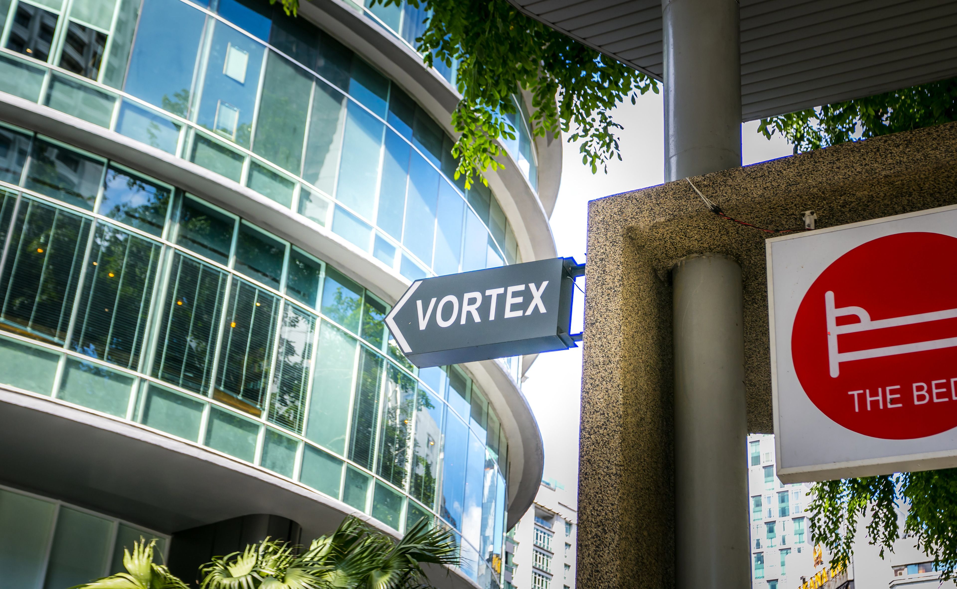A modern building with a glass facade and a sign pointing to "VORTEX".