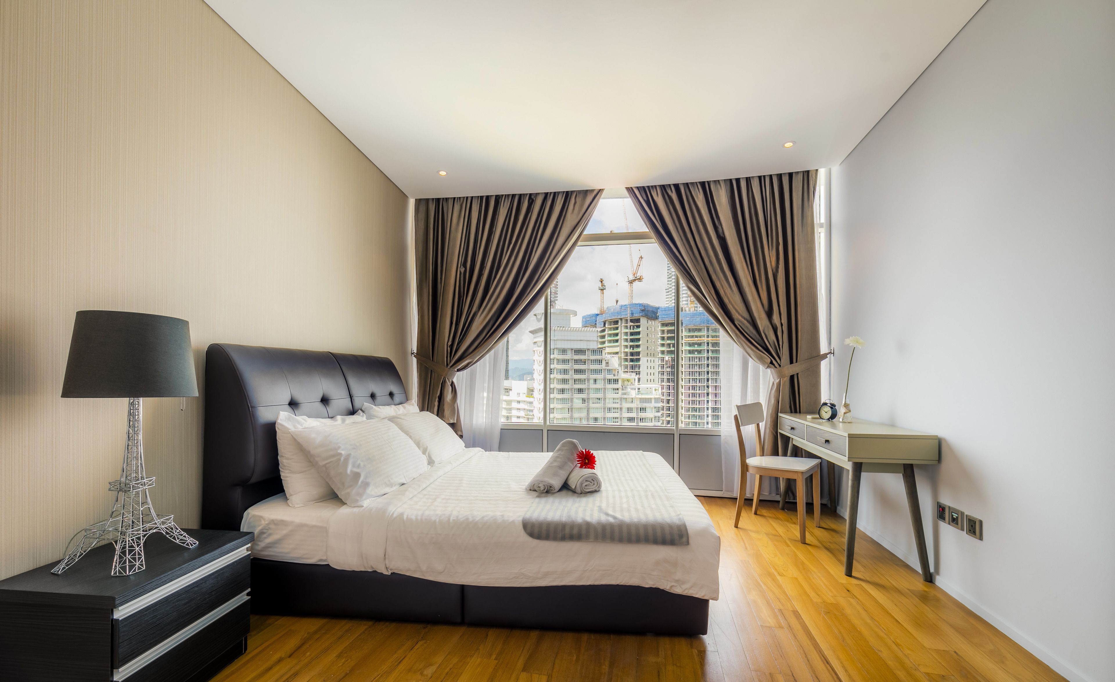 A modern hotel room with a large bed, a desk, and a view of the cityscape.