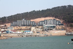 A hotel with multiple floors and a modern design, located near a body of water with boats and a rocky shoreline. - Ritz Castle Resort (Taean)