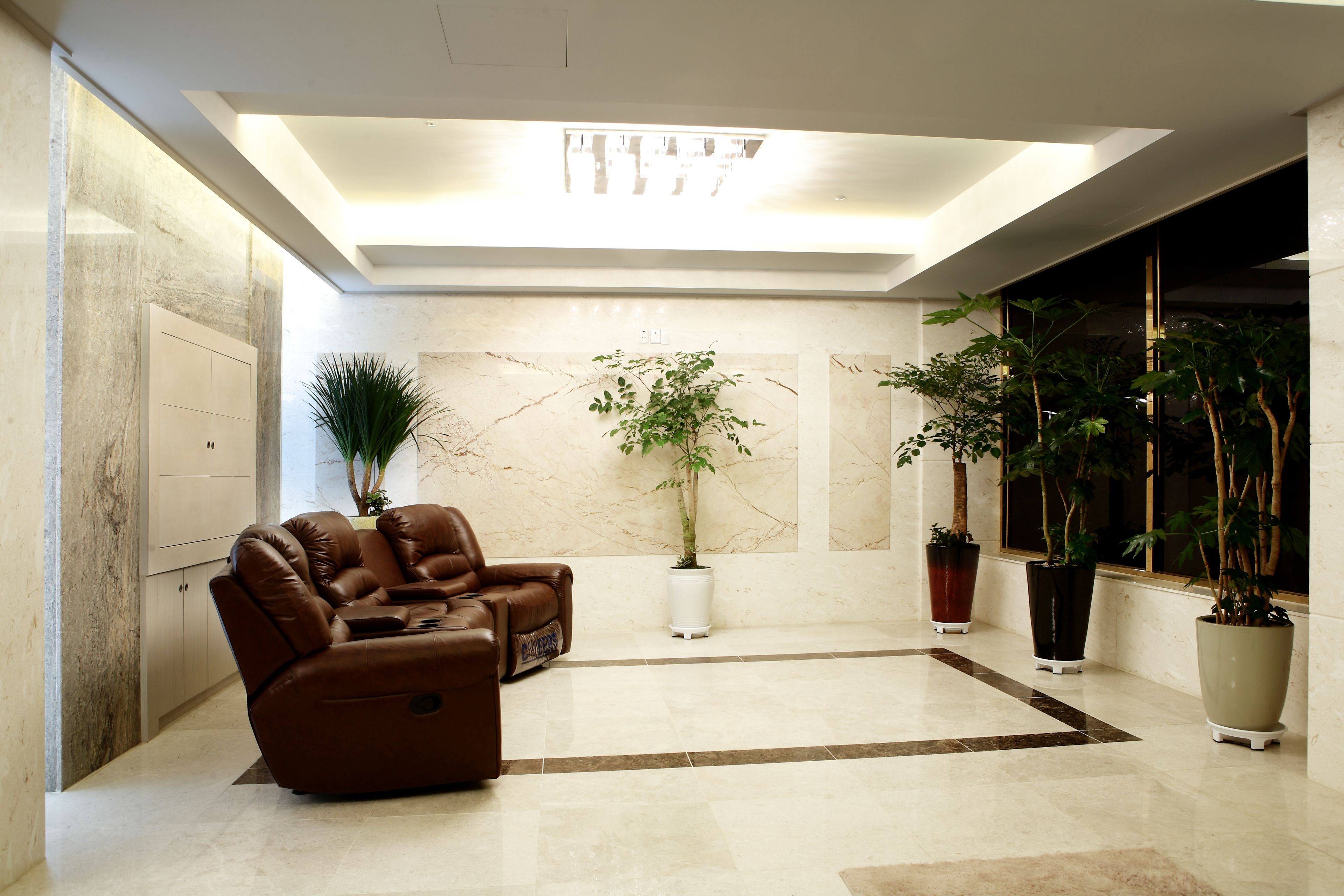 A modern lobby with a leather sofa, marble walls, and potted plants.