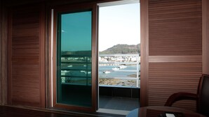 Una habitación con un gran ventanal corredero que da a un balcón con vistas a un río y edificios.