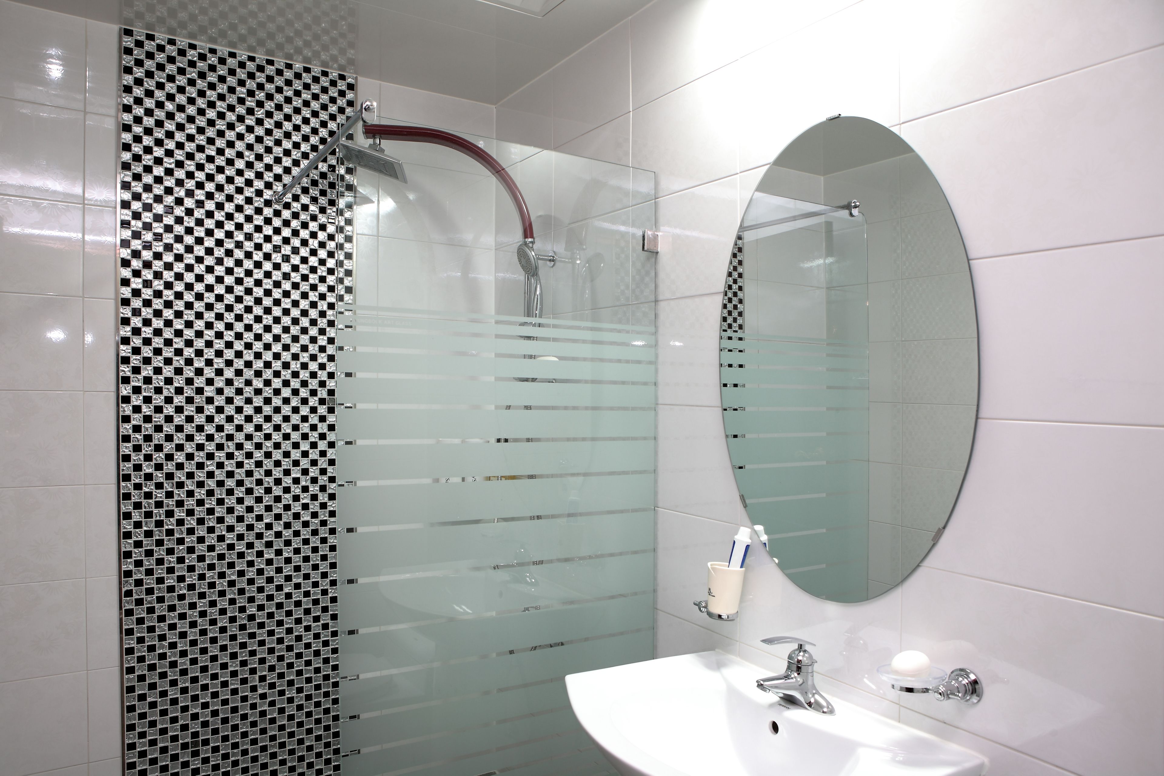 A modern bathroom with a glass shower enclosure, a white sink, and a large oval mirror.
