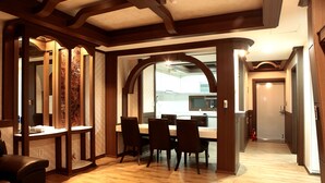 Un comedor amplio con una mesa y sillas de madera, una cocina visible a través de un arco, y un pasillo que lleva a una puerta.