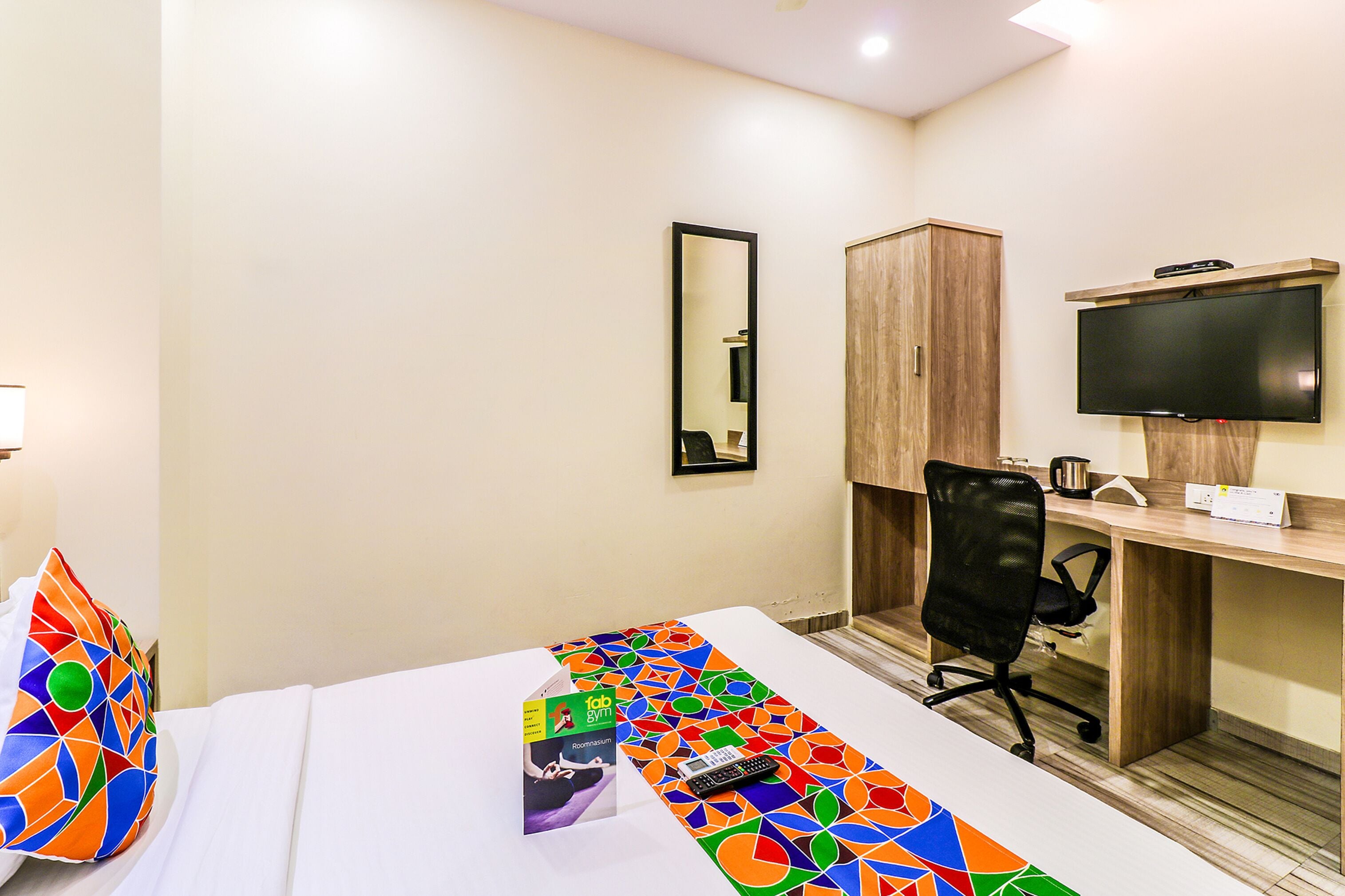 A hotel room with a bed, a desk, a chair, a television, and a mirror.