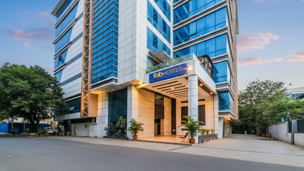 Un hôtel moderne, reconnaissable à son enseigne « FabHotels » bien visible, doté d’une façade en verre et d’une entrée structurée avec des colonnes.