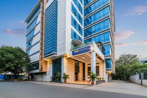 Un moderno edificio de hotel con un llamativo letrero de 'FabHotels', que cuenta con fachada de vidrio y una entrada estructurada con columnas.