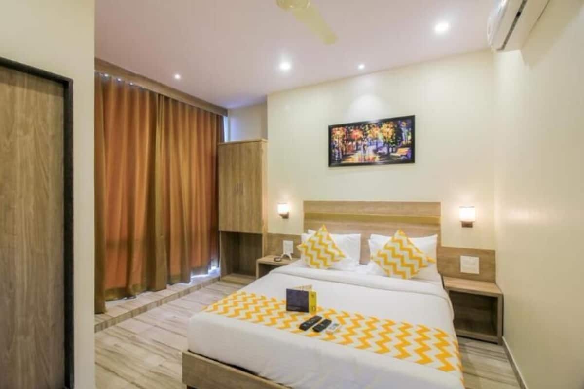 Une chambre d’hôtel avec un lit, deux tables de chevet, une commode, un tableau au mur et une fenêtre avec des rideaux.
