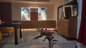 A modern living room with a sofa, a dining table, and a kitchen area with wooden cabinets and a TV. - Samui Villa Whitney (Koh Samui)
