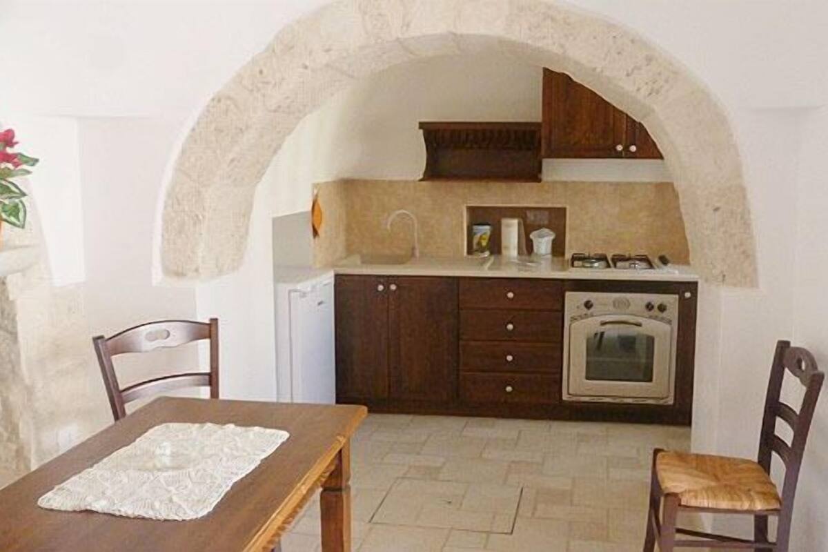 Une cuisine avec une porte en arc de cercle, des meubles de rangement en bois, une cuisinière et un évier.