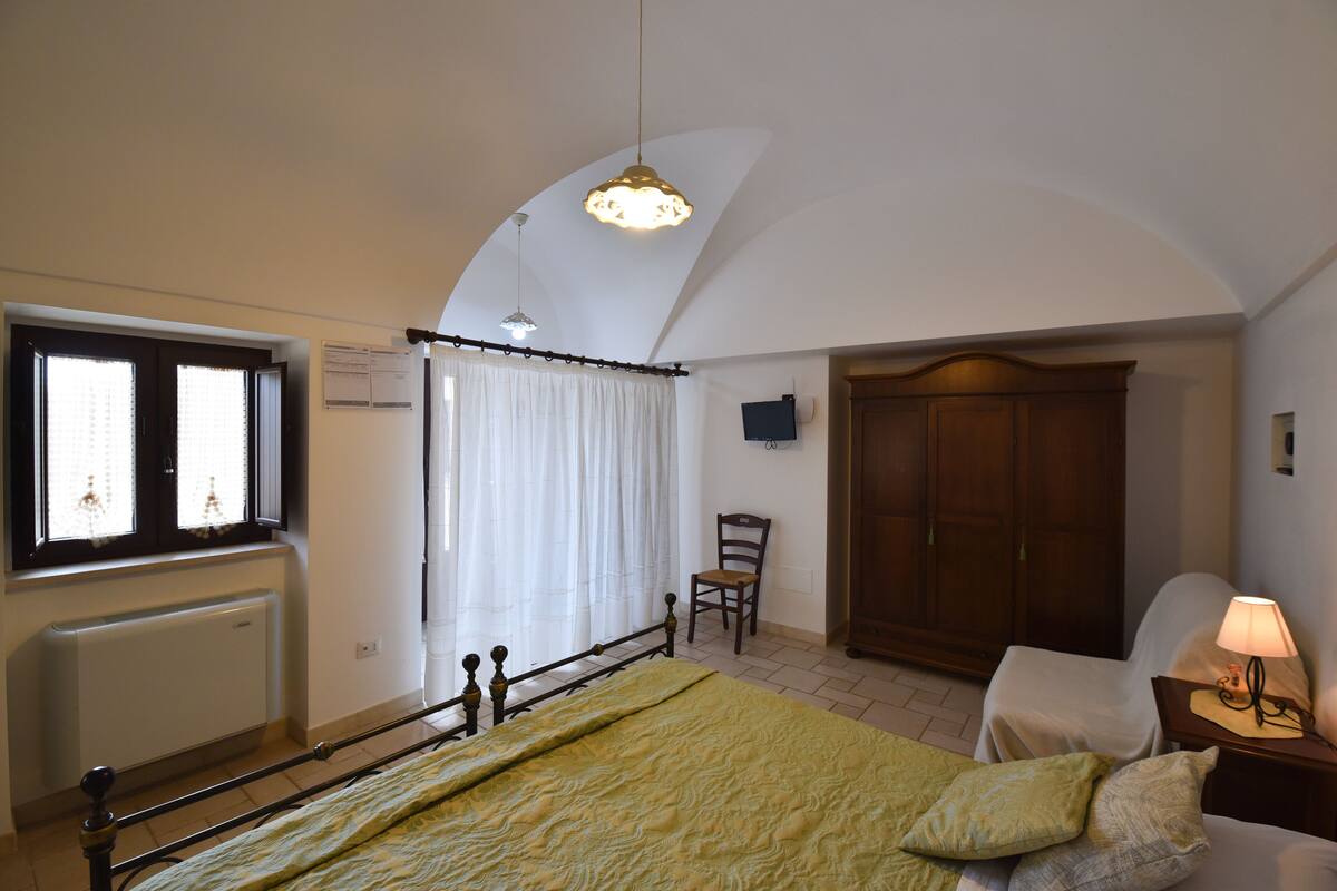Une chambre à coucher comprenant un lit, une chaise, une armoire, un radiateur et une fenêtre avec des rideaux.