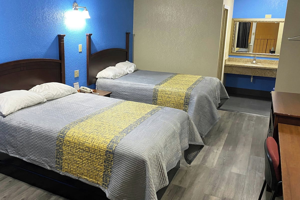 Two double beds with headboards, a bedside phone, a nightstand, a mirror, and a bathroom with a sink and mirror.
