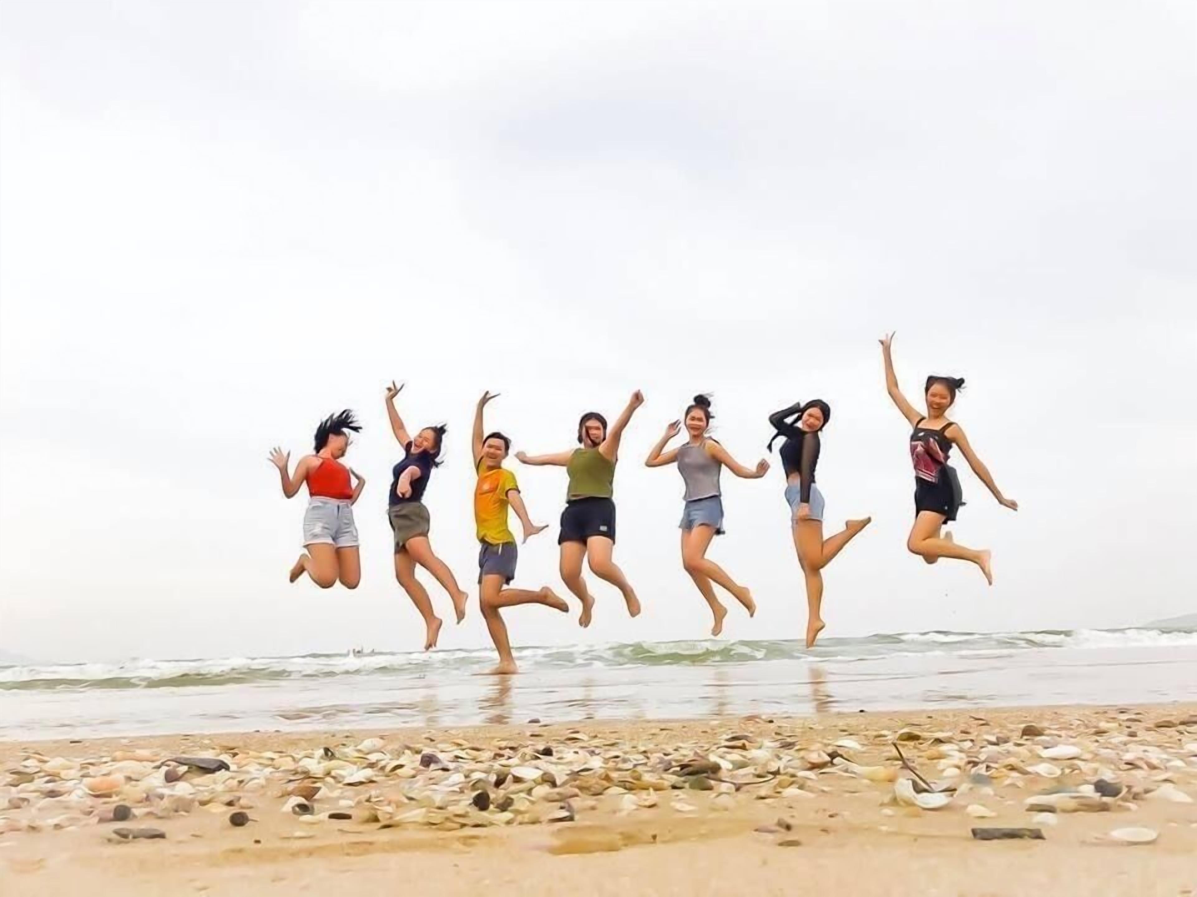 A group of people jumping on a beach with pebbles and the ocean in the background.
