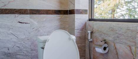 Un baño con pared de mármol, un inodoro y una ventana con vistas a árboles.
