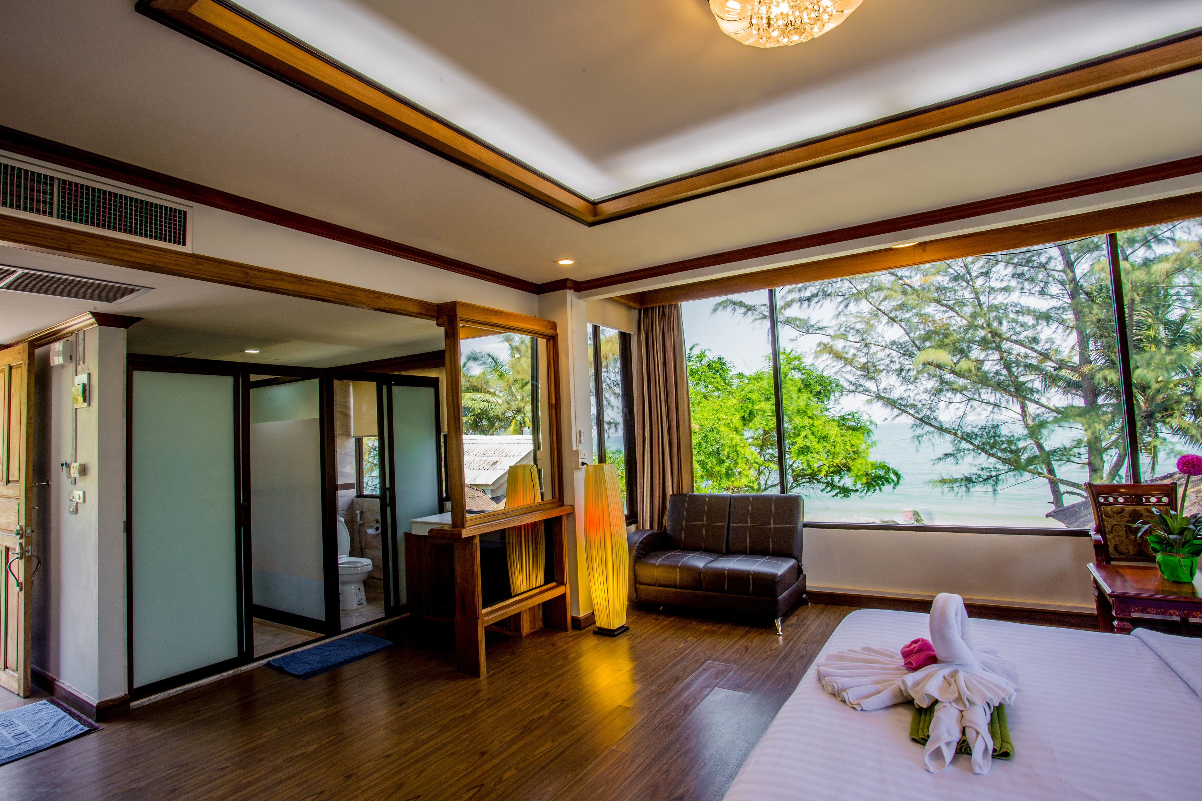 A hotel room with a large bed, a sofa, a desk with a lamp, and a view of the ocean.