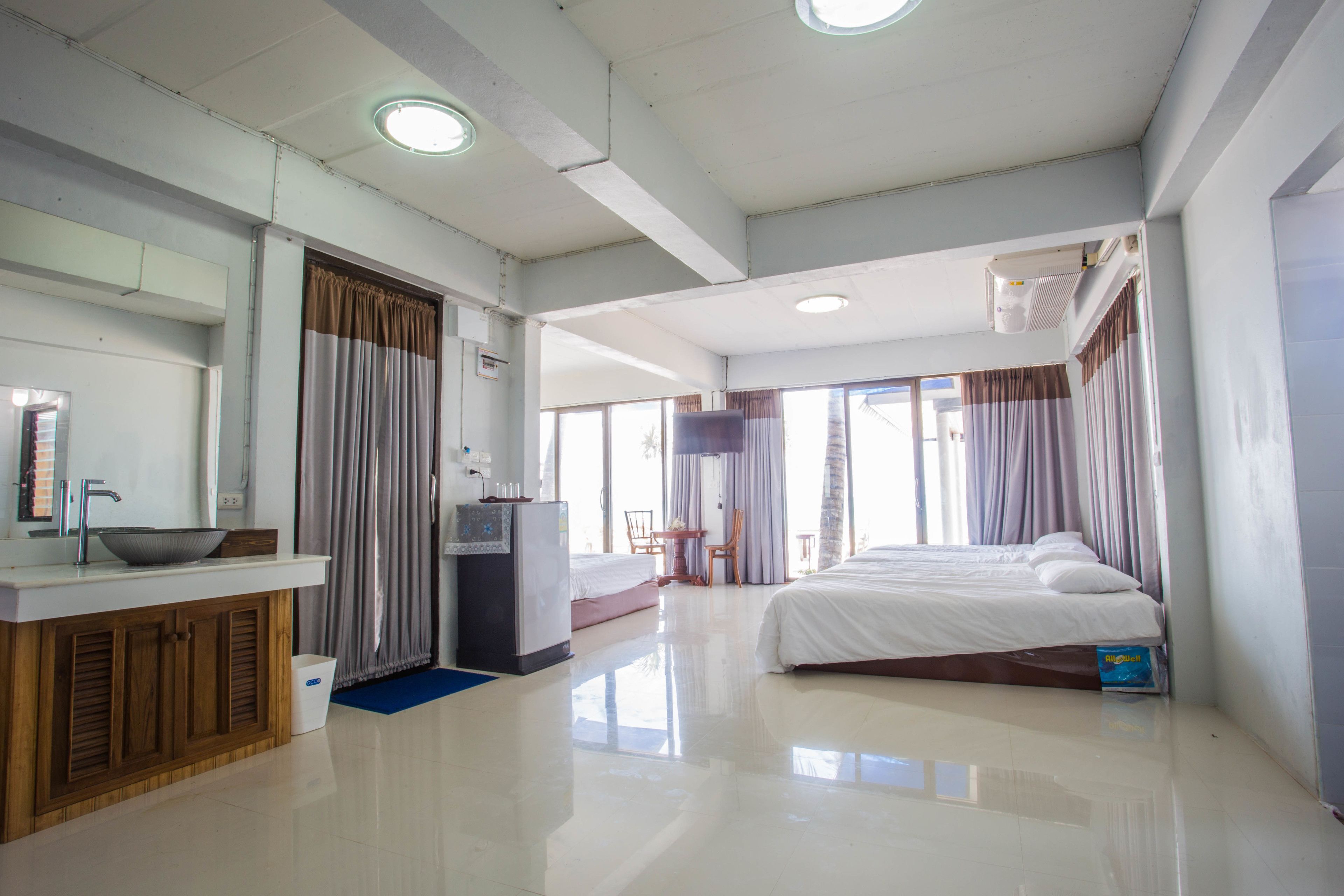 A hotel room with a bed, a desk with a sink, a mirror, and a window with curtains.