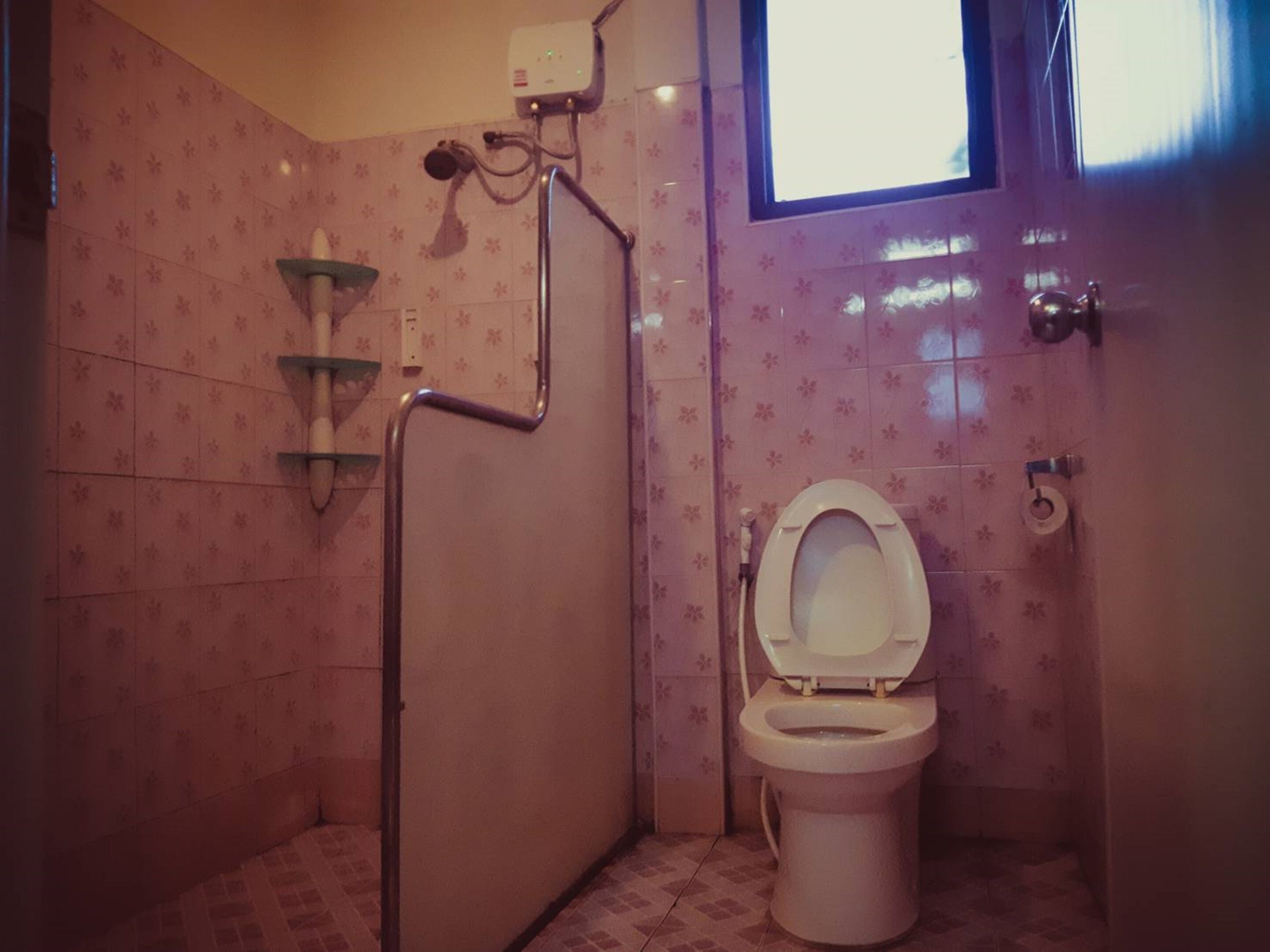 A small bathroom with a toilet, a shower, and a window.