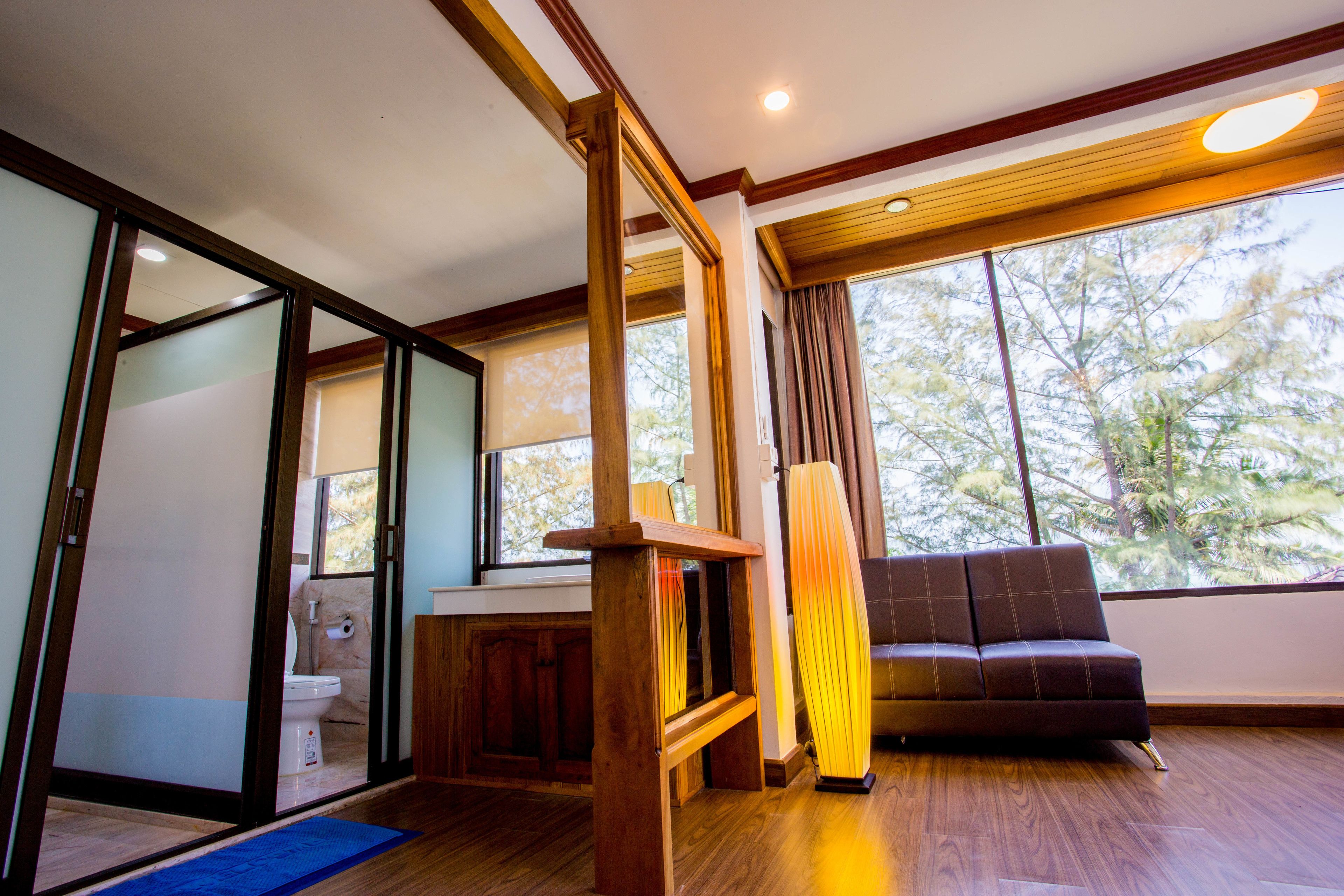 A modern interior with a wooden floor, a sofa, a large window, and a view of trees.