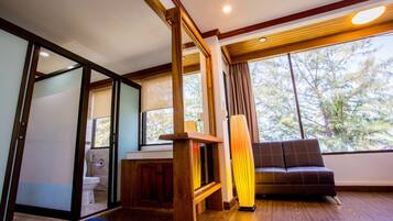 A modern interior with a wooden floor, a sofa, a large window, and a view of trees.