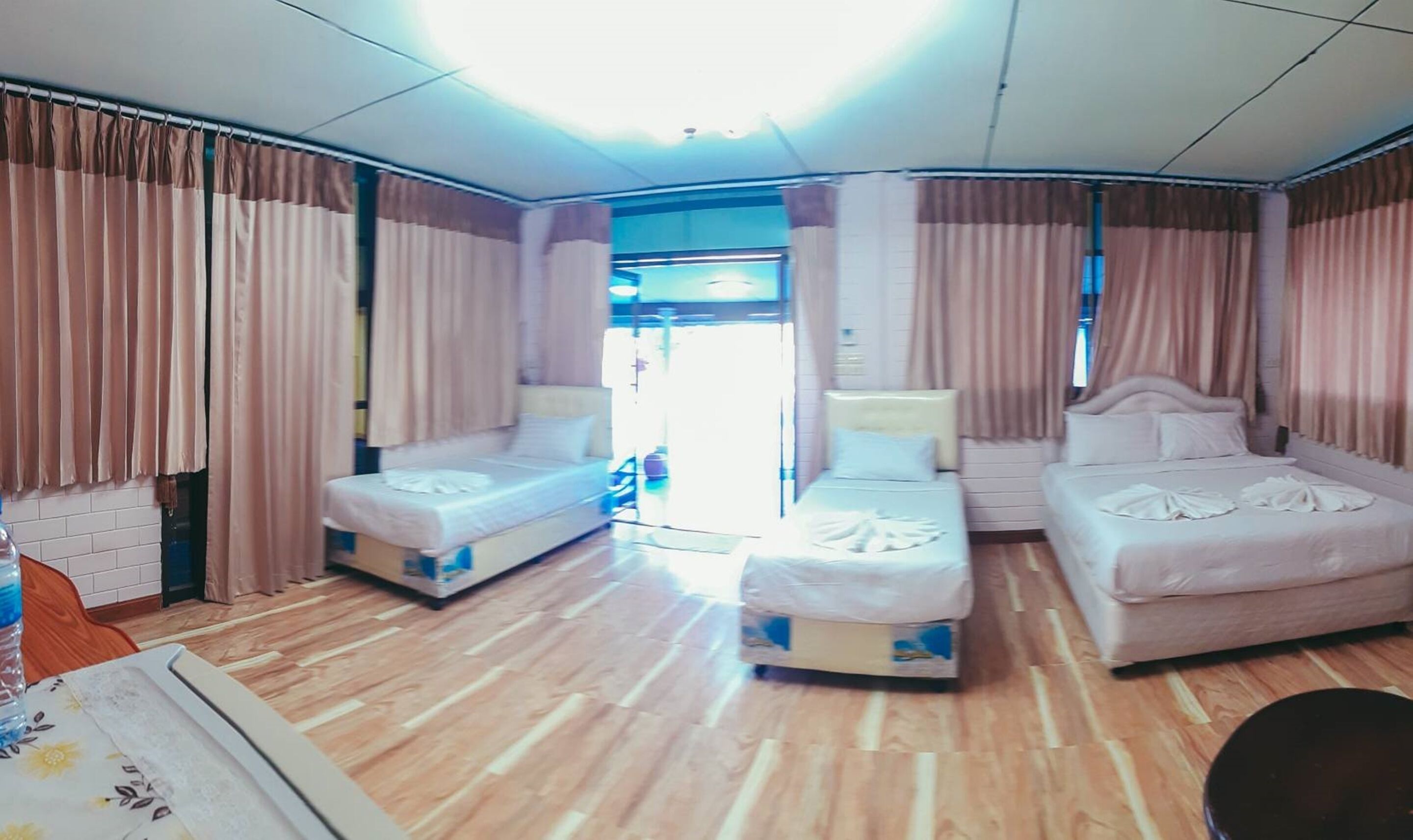 A hotel room with two single beds, a wooden floor, and a large window with curtains.