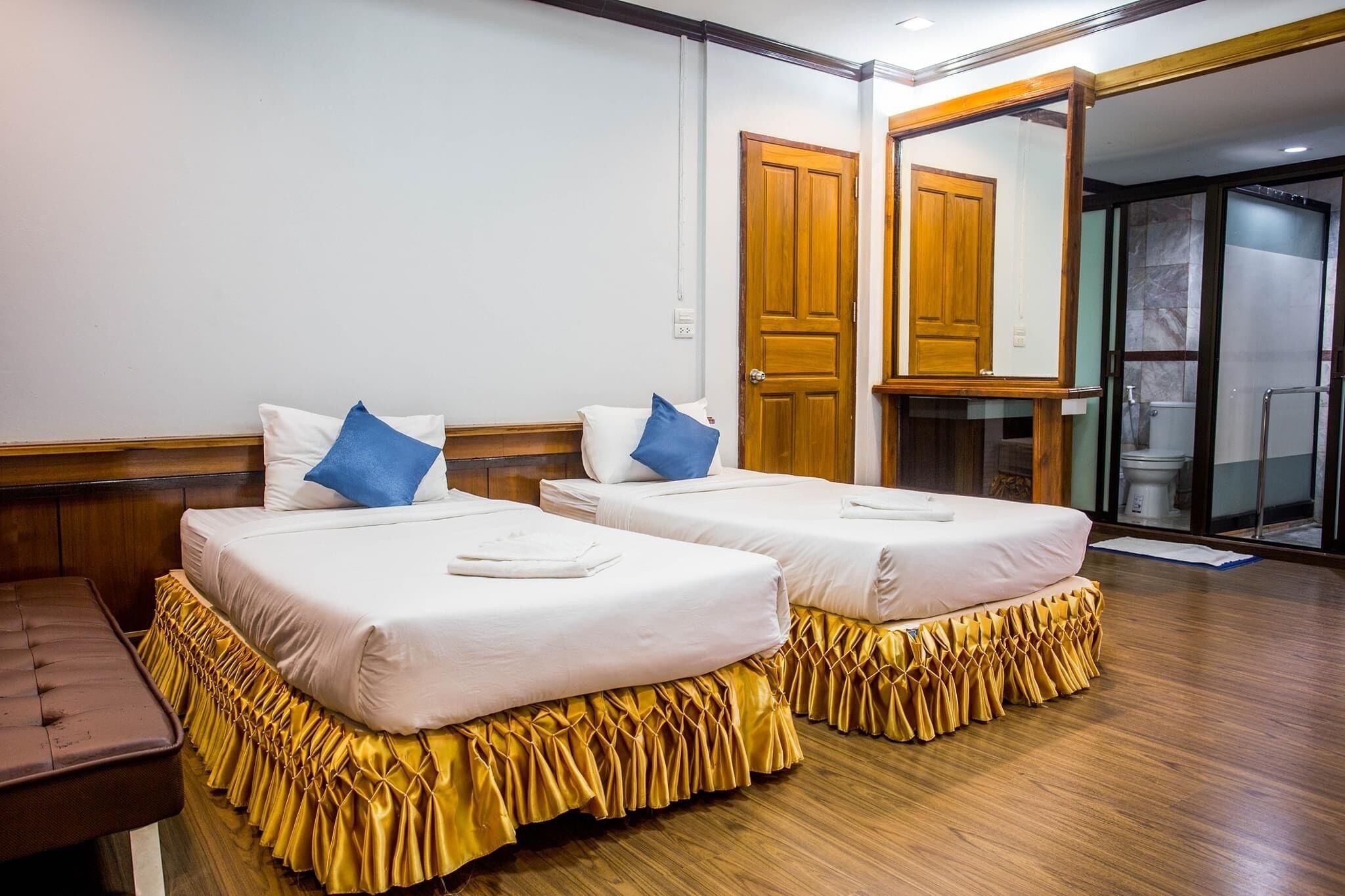 A hotel room with two single beds, a wooden bench, a mirror, and a shower area.