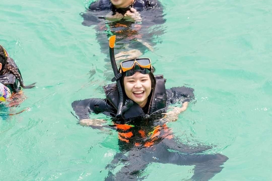 A person in a black wetsuit and snorkel gear swimming in clear water.