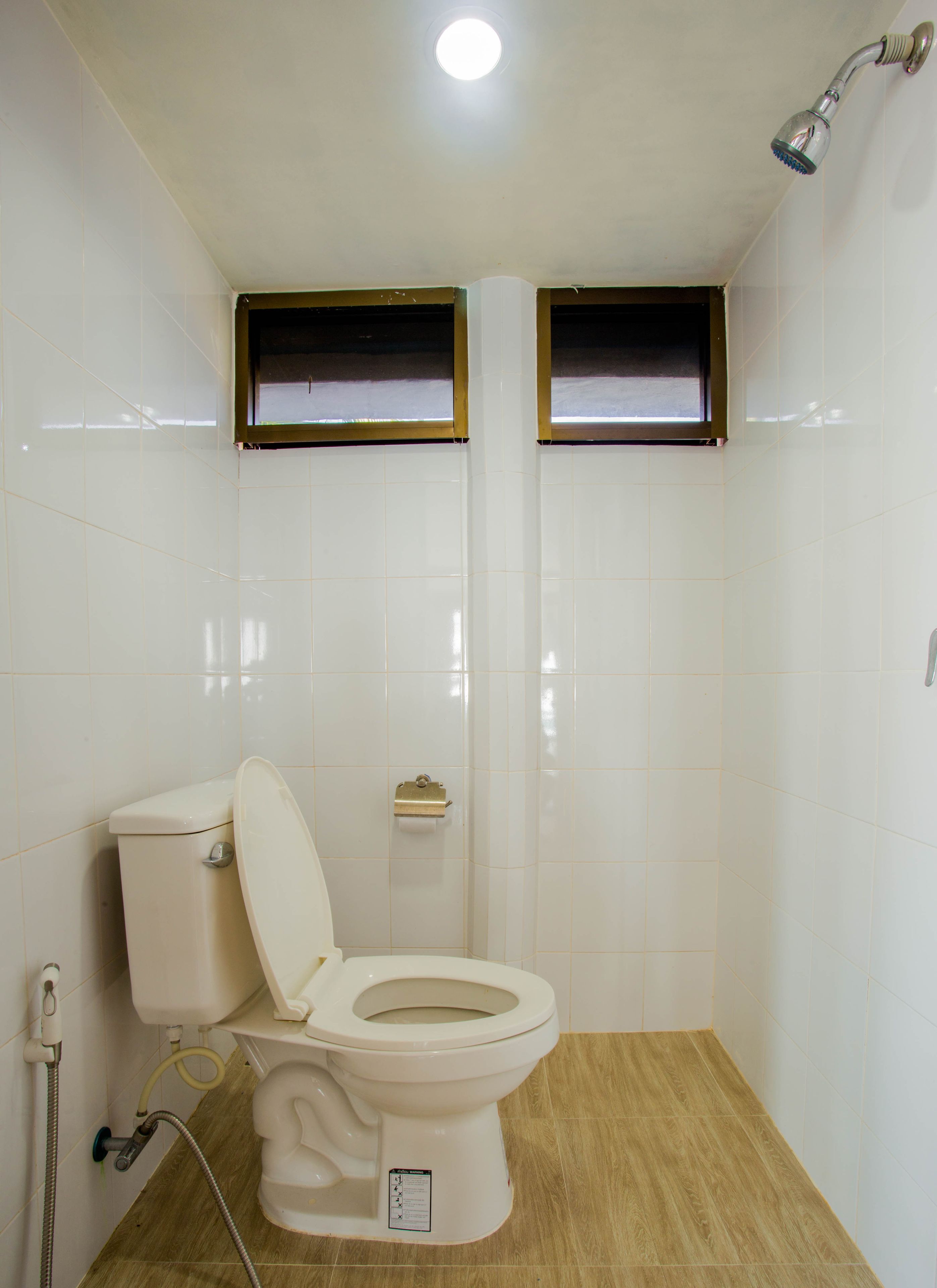Un baño pequeño y funcional con inodoro, cabezal de ducha y ventana sobre el inodoro.