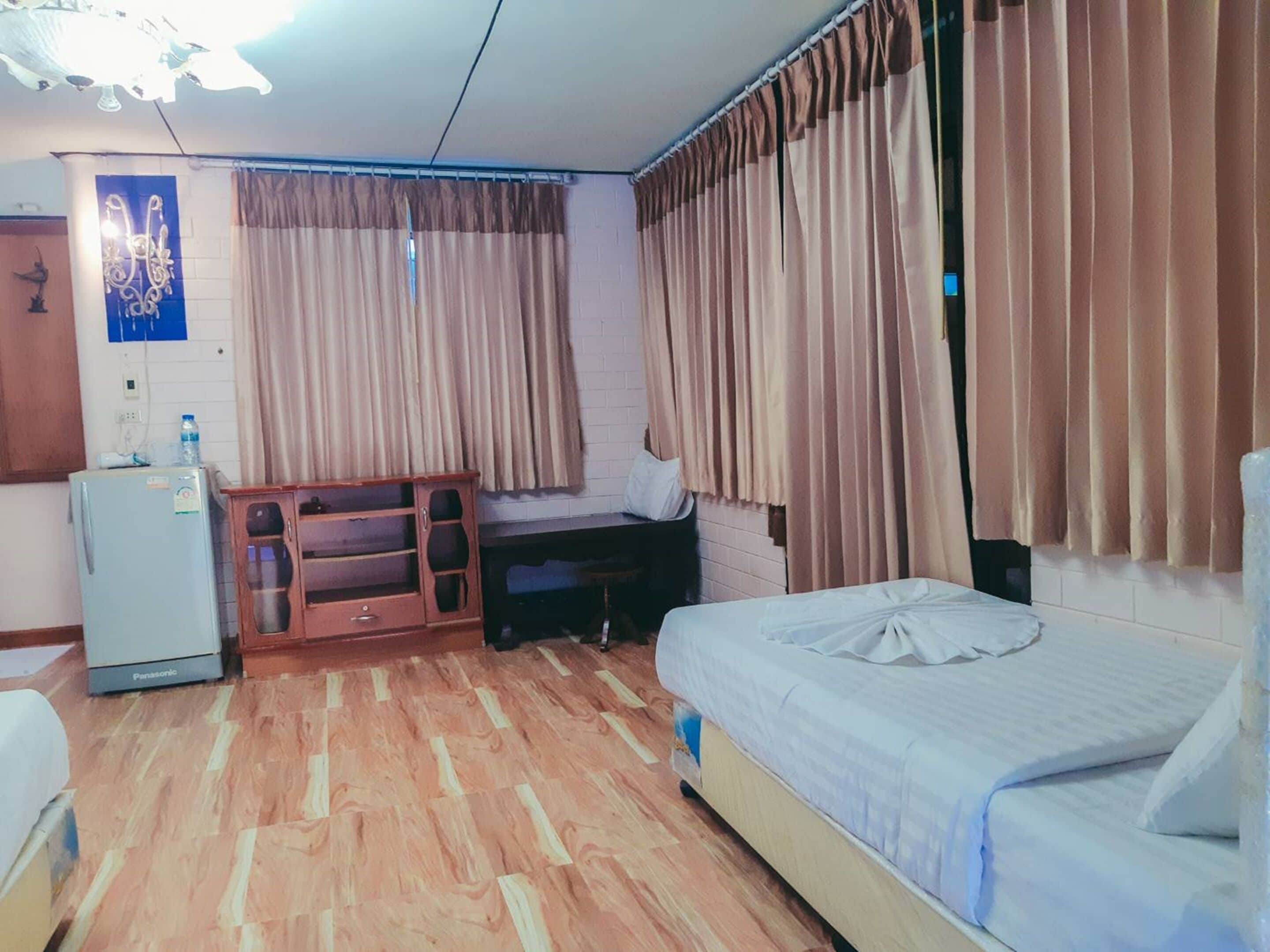 A hotel room with a bed, a desk, a refrigerator, and curtains.