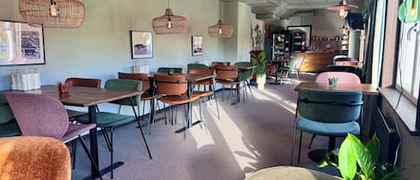 A modern cafe interior with multiple seating arrangements, pendant lighting, and a visible bar area.