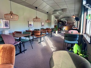 A modern cafe interior with multiple seating arrangements, pendant lighting, and a visible bar area. - Kramfors Stadshotell (Kramfors)