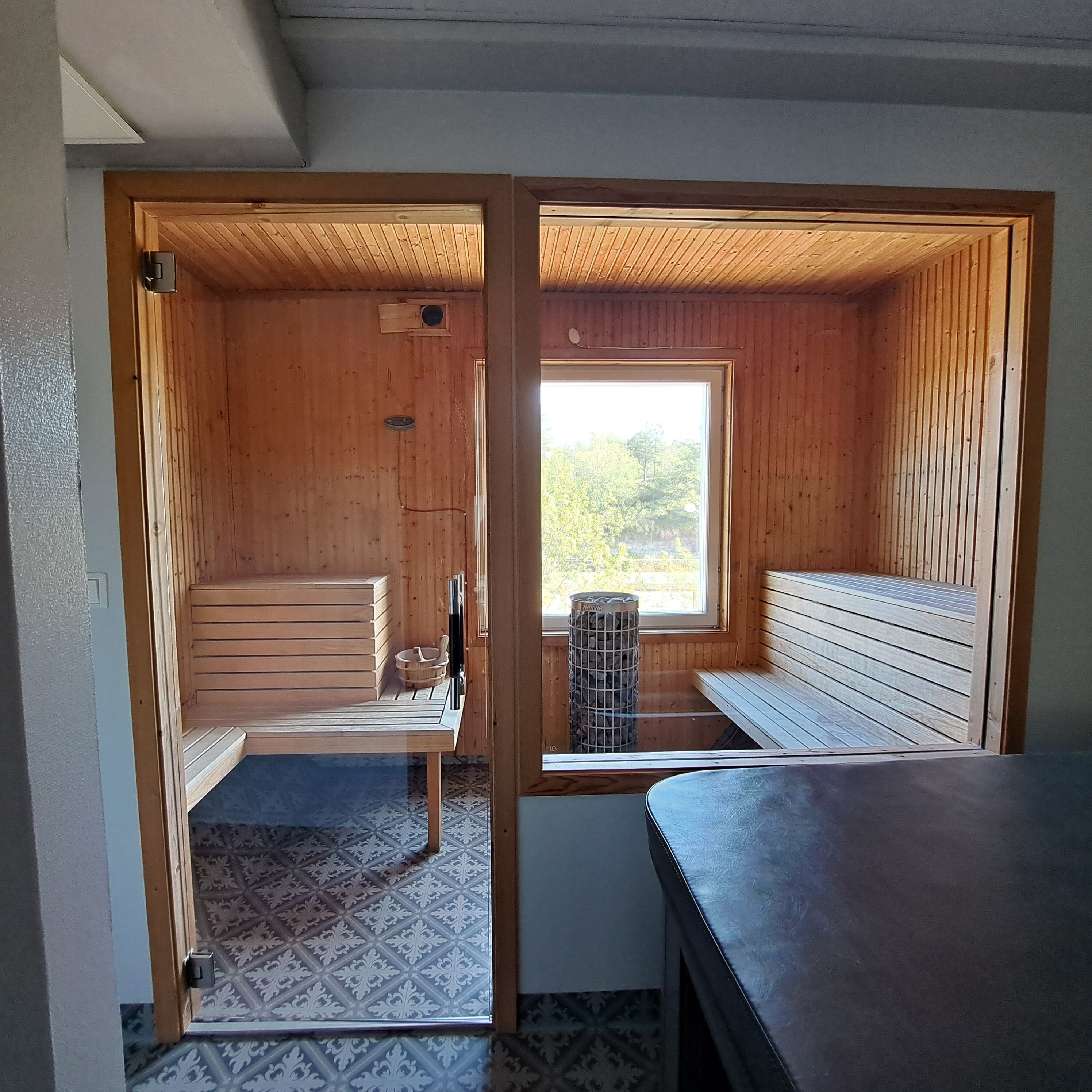 A sauna room with wooden benches and a window providing a view of greenery.