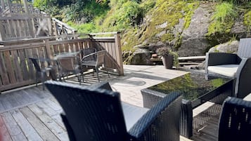 Terraza exterior con mobiliario de mimbre, una mesa de madera y una pared de roca cubierta de musgo.