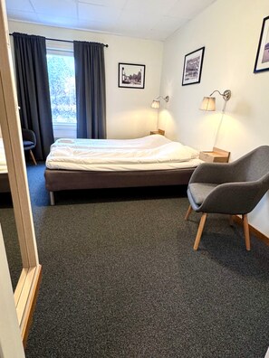 A hotel room with a bed, a chair, a desk, and two wall-mounted lamps. - Kramfors Stadshotell (Kramfors)
